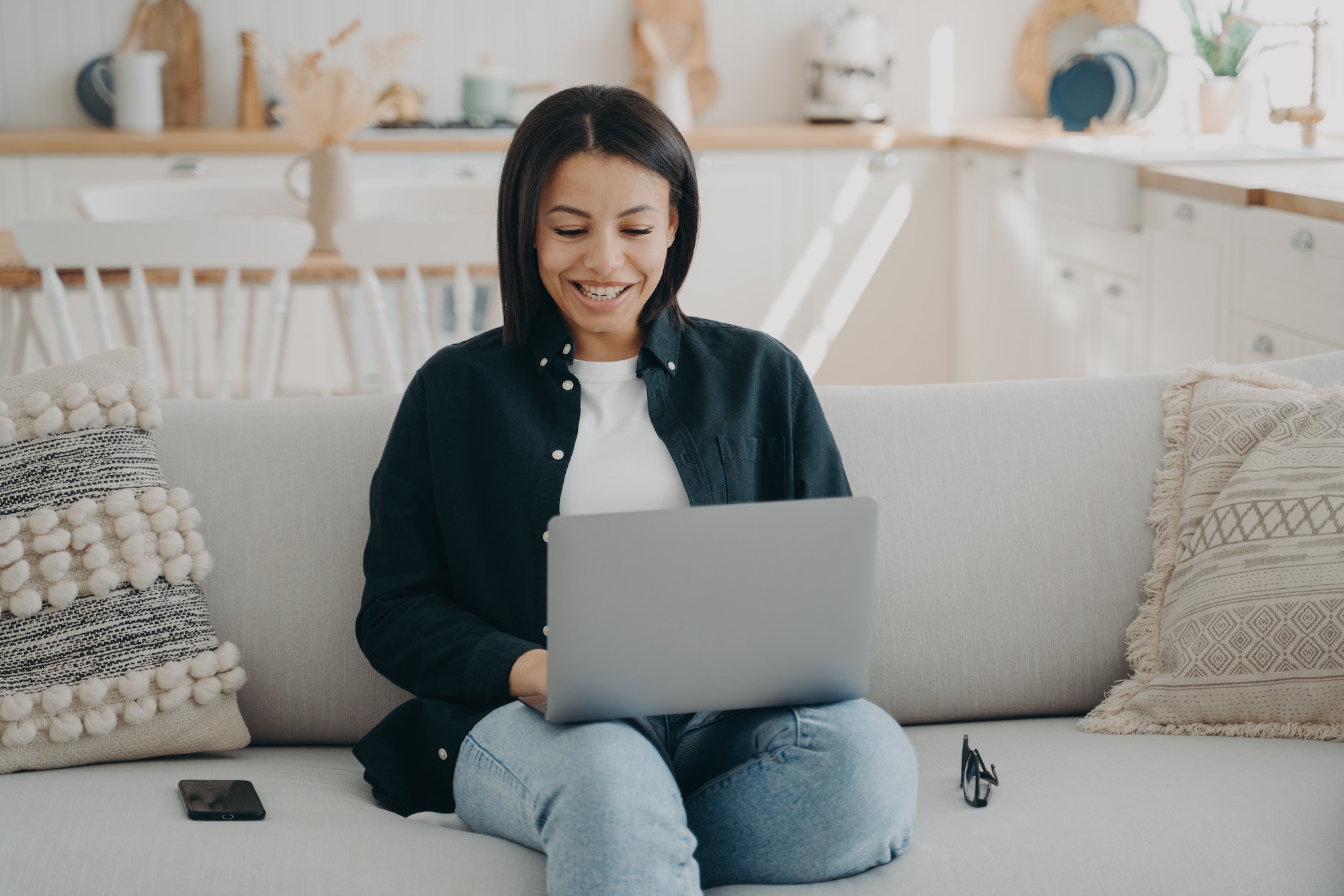 Smiling female shopping on the internet at laptop sitting on couch at home. Ecommerce, online store