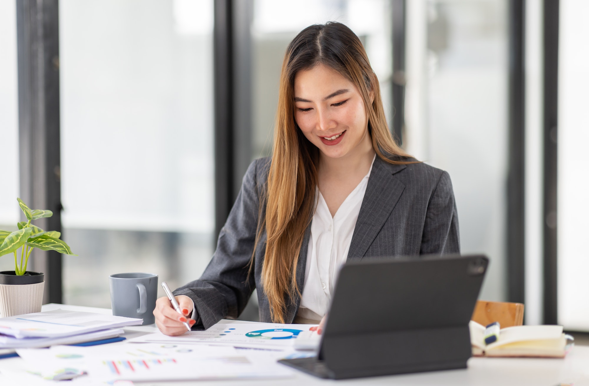 Young business Asian woman is sitting at table, working on laptop with graphs, charts, money